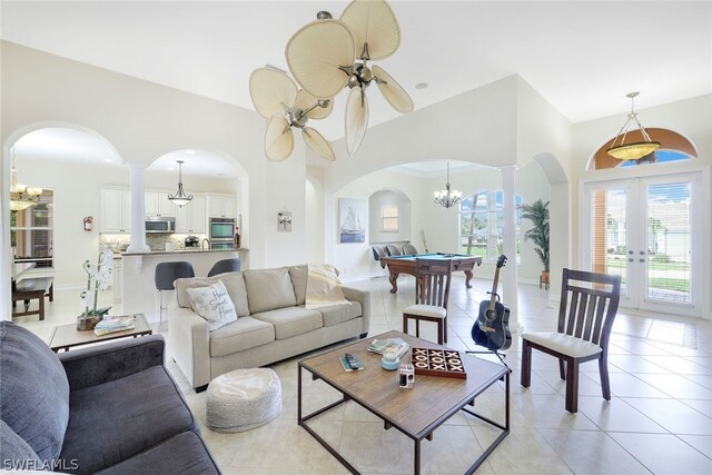 living room featuring ceiling fan with notable chandelier, french doors, ornate columns, and light tile patterned floors