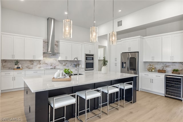 kitchen with wall chimney exhaust hood, sink, white cabinets, wine cooler, and a large island