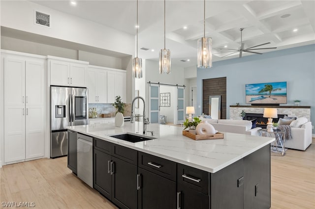 kitchen featuring sink, hanging light fixtures, a barn door, a center island with sink, and appliances with stainless steel finishes