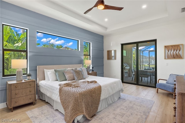 bedroom featuring access to outside, light hardwood / wood-style flooring, ceiling fan, and a tray ceiling