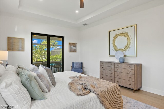 bedroom featuring access to outside, ceiling fan, a tray ceiling, and light hardwood / wood-style floors