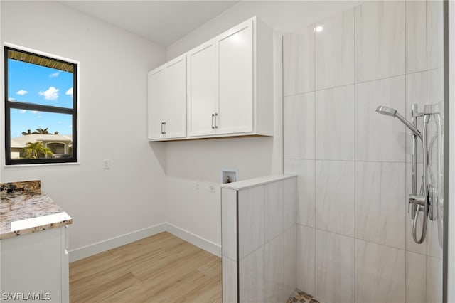 clothes washing area with hookup for a washing machine, cabinets, and light hardwood / wood-style flooring