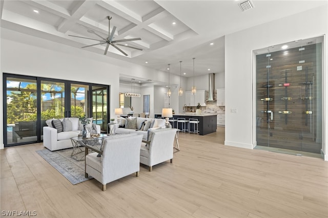 living room with ceiling fan, a high ceiling, coffered ceiling, light hardwood / wood-style flooring, and beamed ceiling