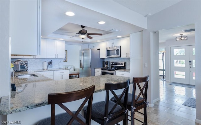 kitchen featuring appliances with stainless steel finishes, white cabinetry, a kitchen breakfast bar, a raised ceiling, and kitchen peninsula