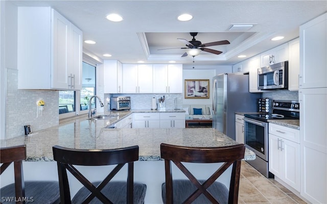 kitchen featuring white cabinetry, appliances with stainless steel finishes, a raised ceiling, and a breakfast bar area