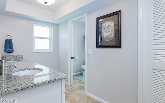 bathroom featuring toilet, a tray ceiling, and vanity