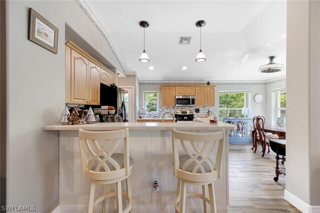 kitchen featuring crown molding, light brown cabinets, appliances with stainless steel finishes, light hardwood / wood-style flooring, and backsplash