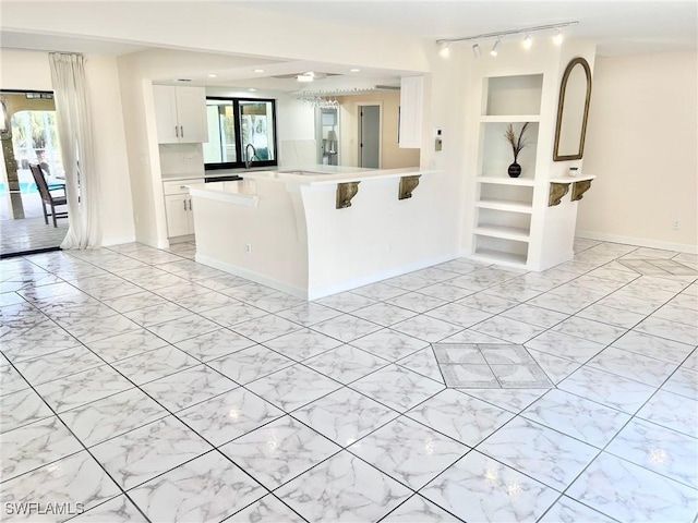 kitchen with sink, a breakfast bar, track lighting, white cabinets, and kitchen peninsula