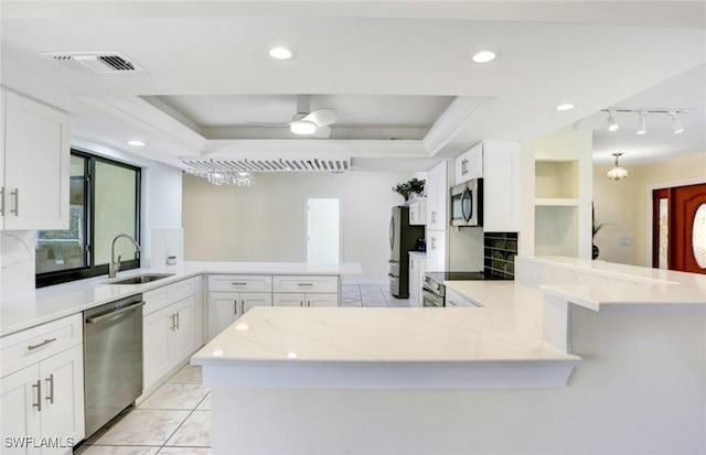 kitchen featuring sink, appliances with stainless steel finishes, white cabinetry, a raised ceiling, and kitchen peninsula