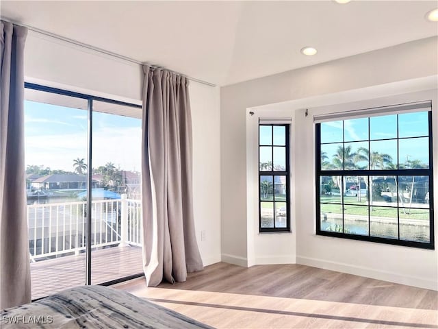 unfurnished bedroom featuring multiple windows, access to exterior, light hardwood / wood-style floors, and a water view