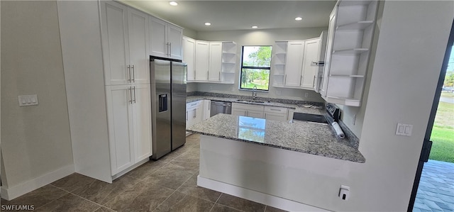 kitchen with kitchen peninsula, white cabinets, appliances with stainless steel finishes, dark tile patterned flooring, and stone countertops