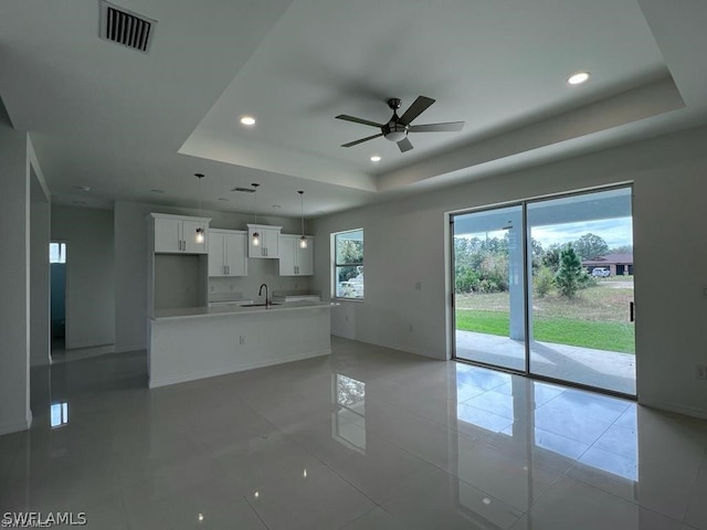 unfurnished living room with a tray ceiling, ceiling fan, light tile patterned floors, and sink