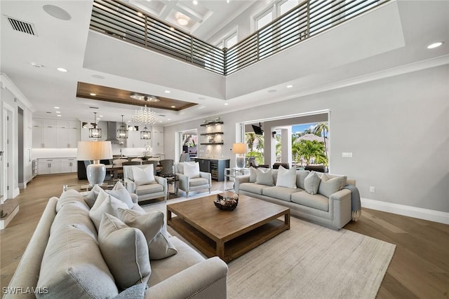 living room with a raised ceiling, crown molding, light hardwood / wood-style flooring, a chandelier, and a high ceiling