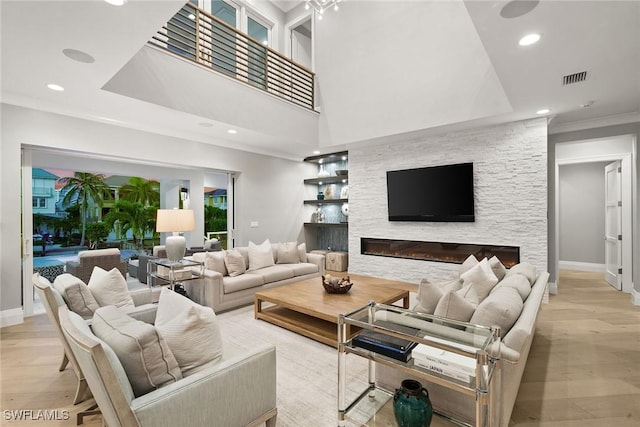 living room featuring a stone fireplace, crown molding, and light hardwood / wood-style flooring