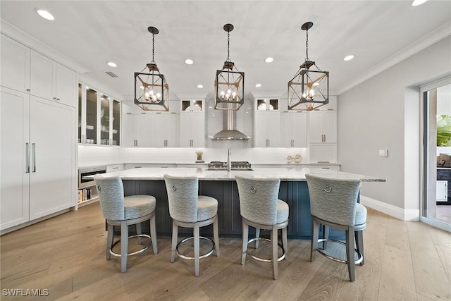 kitchen featuring hanging light fixtures, light wood-type flooring, an island with sink, ornamental molding, and white cabinetry