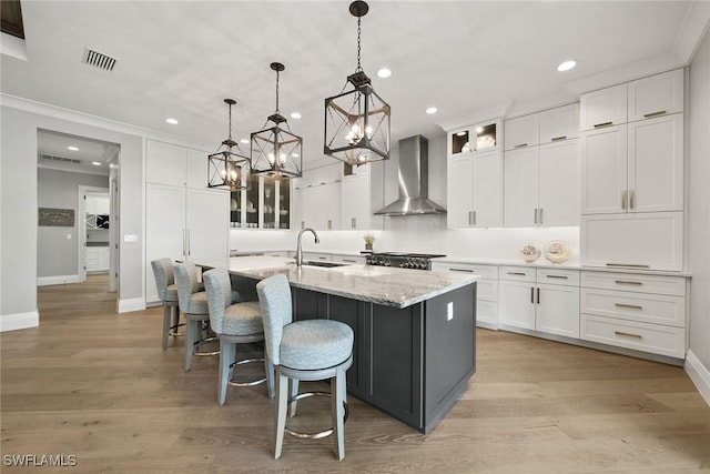 kitchen featuring white cabinets, wall chimney exhaust hood, a kitchen island with sink, and hanging light fixtures