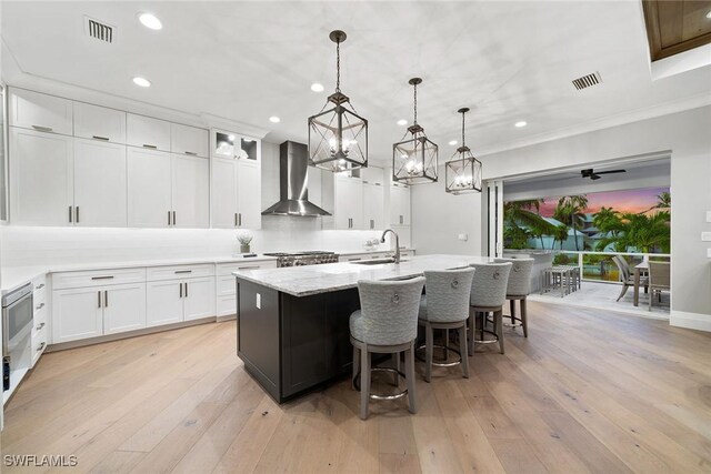 175 Conners Ave, Naples, FL 34108 - kitchen featuring wall chimney range hood, a sink, a kitchen island with sink, recessed lighting, and white cabinetry