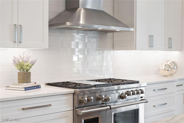 kitchen featuring white cabinetry, range with two ovens, wall chimney range hood, and backsplash