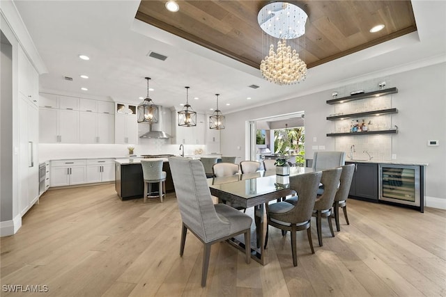 dining area with light hardwood / wood-style floors, a raised ceiling, beverage cooler, and an inviting chandelier