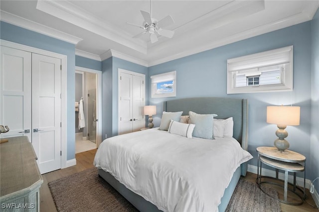 bedroom with ceiling fan, ornamental molding, a tray ceiling, multiple windows, and wood-type flooring