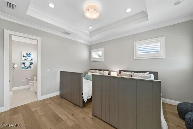 bedroom with light wood-type flooring, a tray ceiling, crown molding, and ensuite bathroom