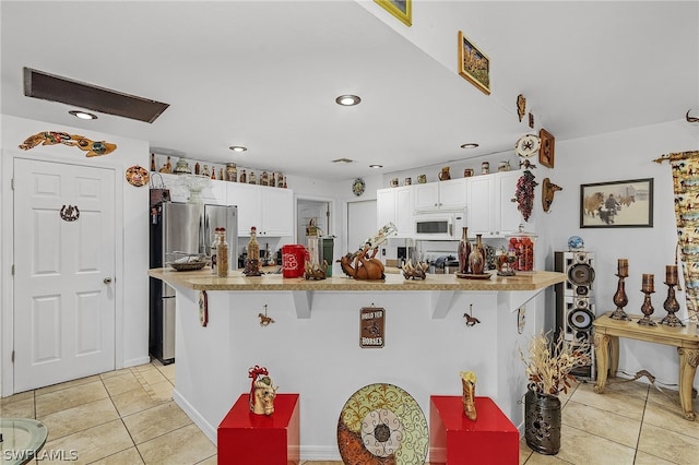 kitchen featuring white cabinetry, a breakfast bar, stainless steel fridge, and light tile patterned floors