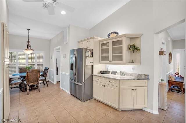 kitchen with stainless steel refrigerator with ice dispenser, light tile patterned floors, light stone counters, and cream cabinets