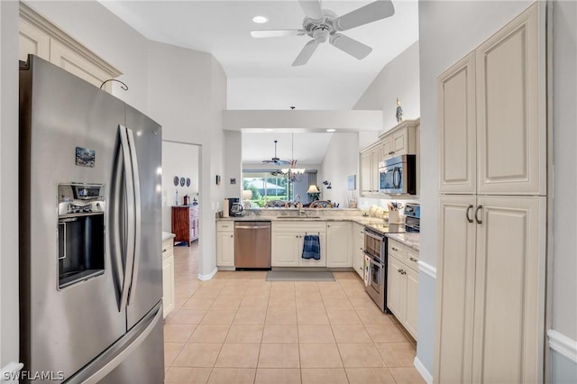 kitchen featuring lofted ceiling, sink, appliances with stainless steel finishes, light tile patterned floors, and ceiling fan with notable chandelier