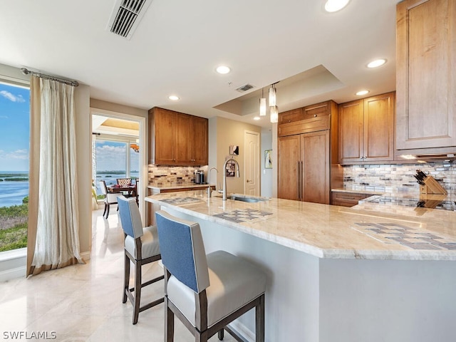 kitchen featuring paneled fridge, tasteful backsplash, kitchen peninsula, a raised ceiling, and light stone countertops