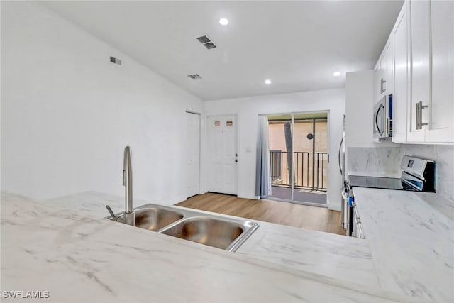 kitchen with light stone counters, stainless steel appliances, vaulted ceiling, sink, and white cabinets