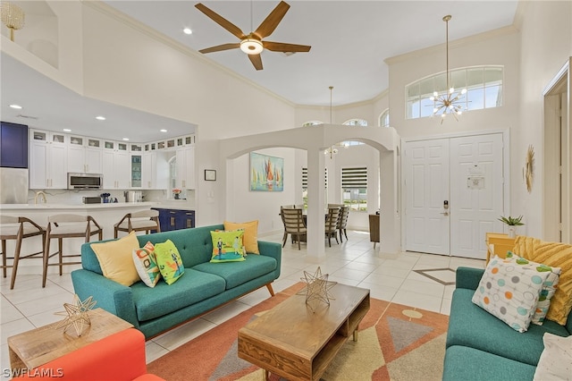 tiled living room featuring ceiling fan with notable chandelier, a healthy amount of sunlight, a towering ceiling, and ornamental molding