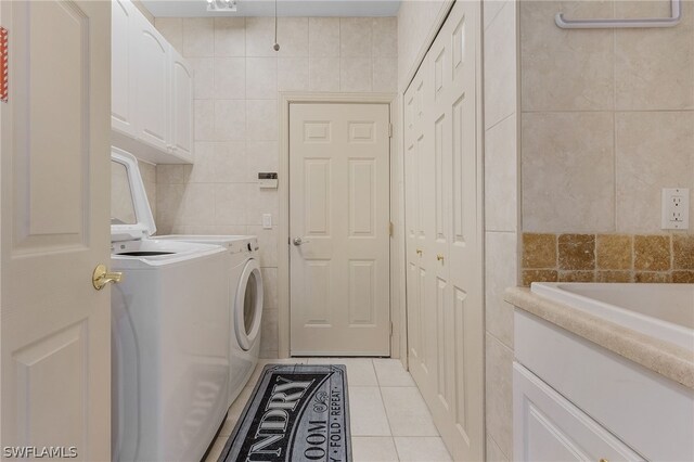 laundry area with washing machine and clothes dryer, light tile patterned flooring, cabinets, and tile walls