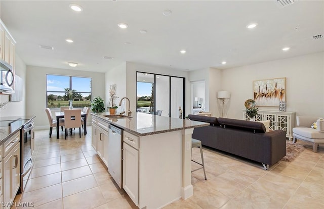 kitchen featuring light stone countertops, stainless steel appliances, an island with sink, sink, and a breakfast bar area