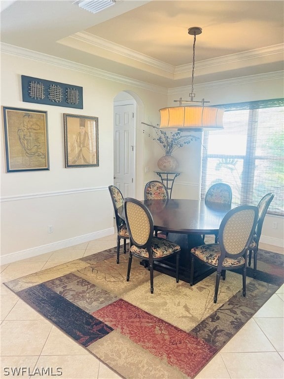 tiled dining room with ornamental molding and a raised ceiling