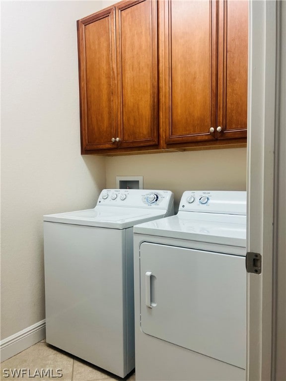 clothes washing area with cabinets, washer and dryer, and light tile patterned floors