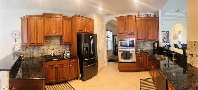 kitchen with appliances with stainless steel finishes, light tile patterned floors, dark stone countertops, and decorative backsplash