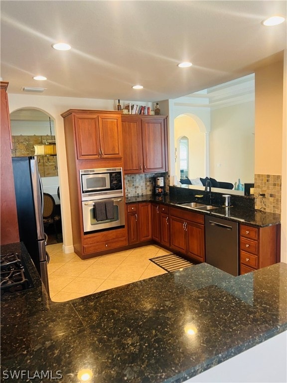 kitchen with tasteful backsplash, stainless steel appliances, sink, light tile patterned floors, and dark stone countertops