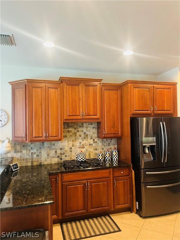 kitchen with tasteful backsplash, light tile patterned flooring, black gas cooktop, stainless steel refrigerator with ice dispenser, and dark stone countertops