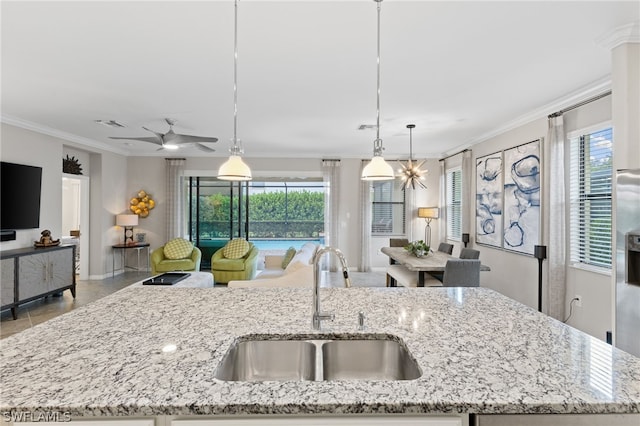 kitchen featuring light stone counters, a center island with sink, hanging light fixtures, and sink