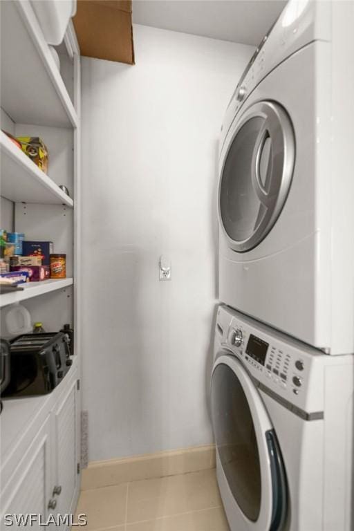 clothes washing area featuring laundry area, stacked washer / dryer, tile patterned floors, and baseboards