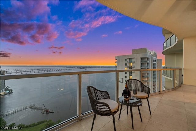 balcony at dusk featuring a water view