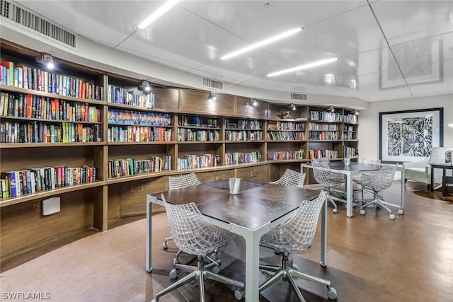 office space featuring concrete flooring, visible vents, and wall of books