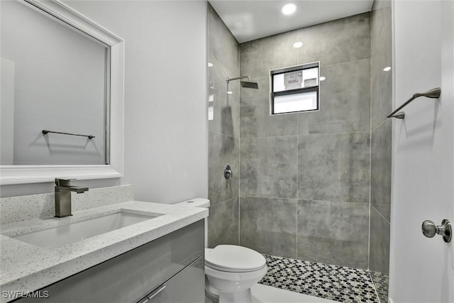 bathroom with a tile shower, toilet, and vanity