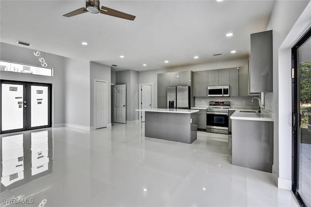 kitchen with gray cabinetry, a center island, light countertops, appliances with stainless steel finishes, and a sink