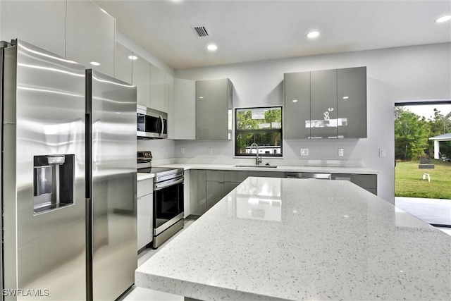 kitchen with gray cabinetry, light stone counters, stainless steel appliances, modern cabinets, and a sink