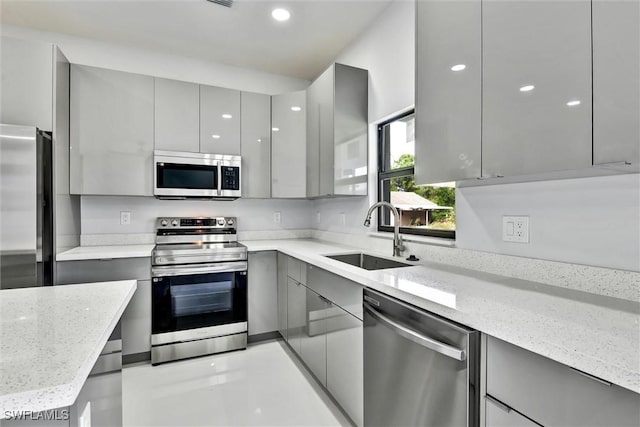 kitchen with light stone counters, a sink, gray cabinetry, appliances with stainless steel finishes, and modern cabinets