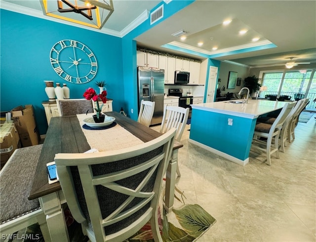 dining space featuring sink, crown molding, light tile patterned flooring, and a tray ceiling