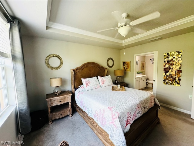 bedroom with multiple windows, ensuite bath, a tray ceiling, and ceiling fan