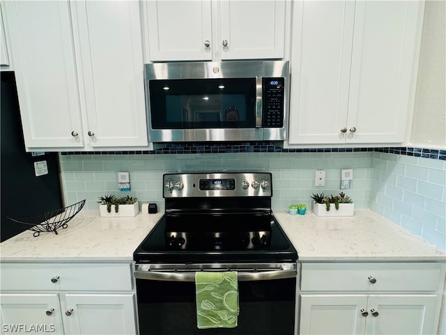 kitchen with light stone countertops, white cabinets, stainless steel appliances, and backsplash