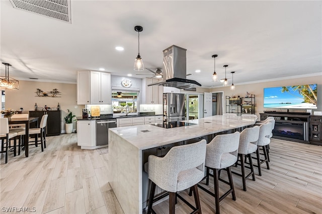 kitchen with decorative light fixtures, a spacious island, white cabinetry, appliances with stainless steel finishes, and island range hood